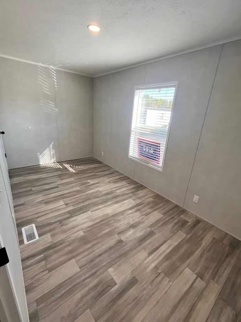 Empty room with wood-look flooring, gray walls, and a window with blinds.