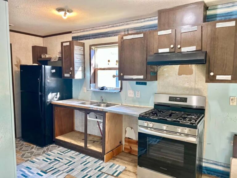 Aging kitchen with wooden cabinets, black refrigerator, and stainless gas stove during renovation