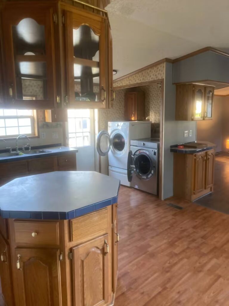 Kitchen with oak cabinets, octagon island, and washer and dryer in alcove with hardwood flooring.