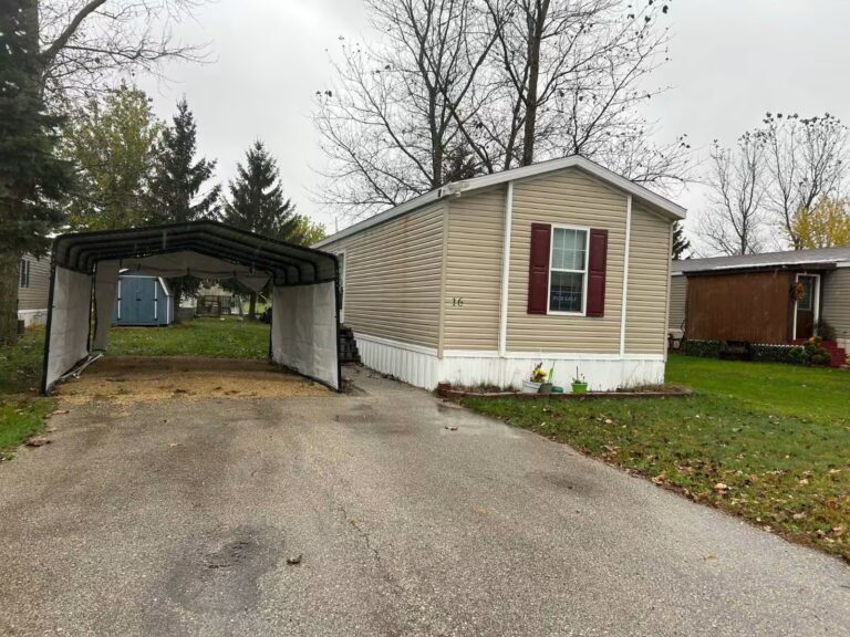 Beige mobile home with maroon shutters, carport, and paved driveway, marked 16.